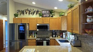 A modern kitchen with granite countertops, stainless steel appliances, wooden cabinets, and decorative plants. - Blackhawk 5BD Home: Hot Tub, Arcade, near Whitworth & Green Bluff (Spokane)