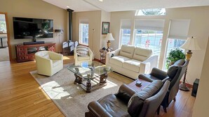 A living room with a flat-screen TV, a fireplace, a sofa, a coffee table, and a window with blinds. - Blackhawk 5BD Home: Hot Tub, Arcade, near Whitworth & Green Bluff (Spokane)