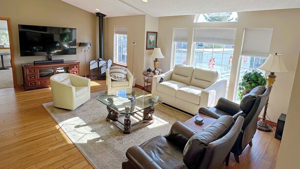 A living room with a flat-screen TV, a fireplace, a sofa, a coffee table, and a window with blinds. - Blackhawk 5BD Home: Hot Tub, Arcade, near Whitworth & Green Bluff (Spokane)