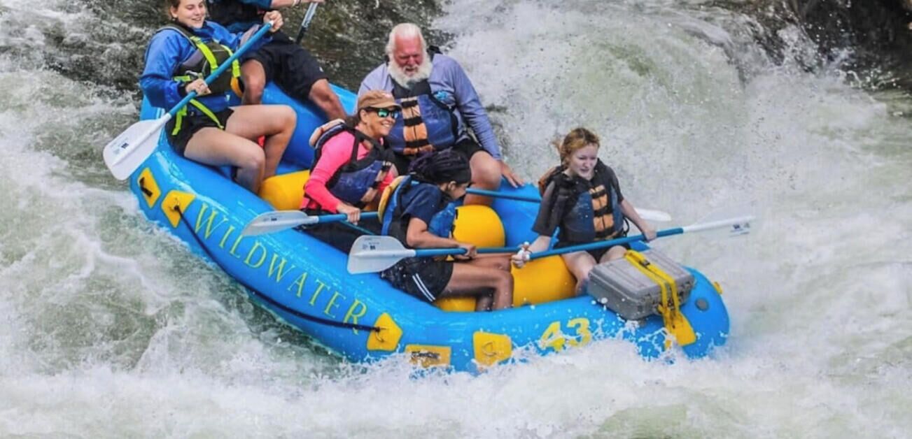 A group of people in a blue inflatable raft labeled 'WILDWATER' navigating a river.