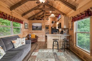 Un intérieur de chalet chaleureux comprenant un espace de vie, une cuisine et de grandes fenêtres.