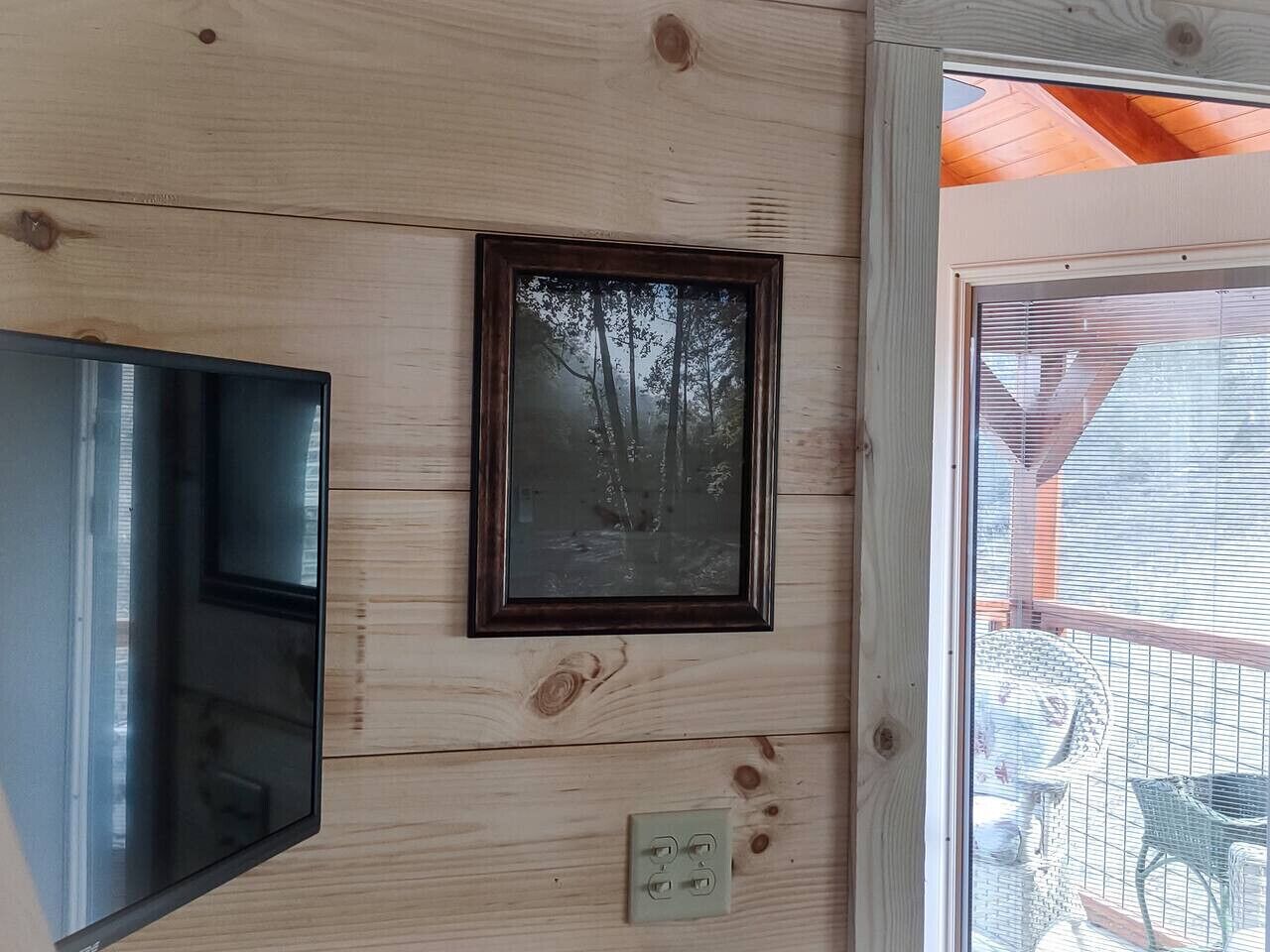 A room with wooden panel walls, a framed picture, a light switch, and a window with blinds.