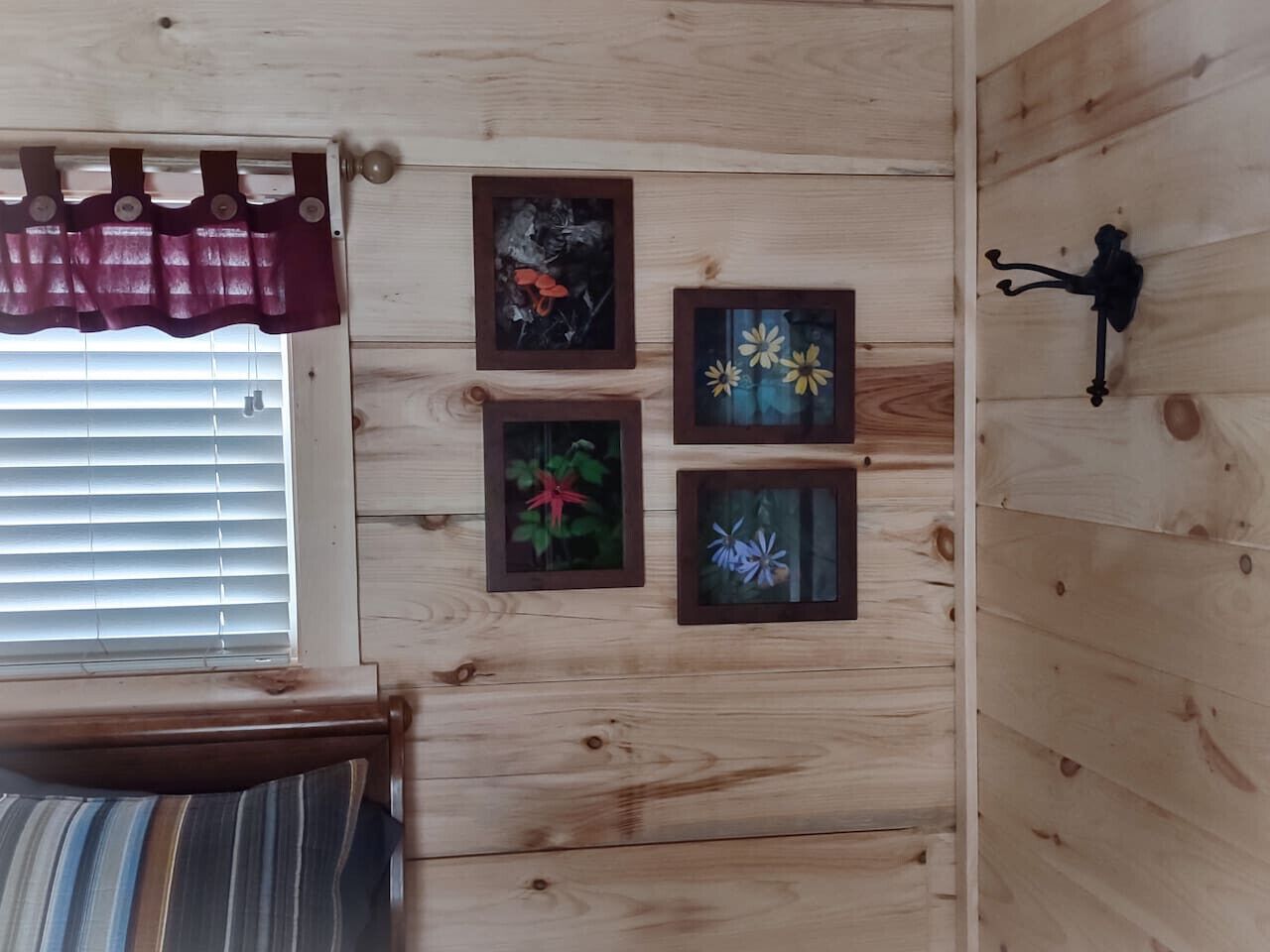 A wooden room with a bed, a window with blinds, and three framed pictures on the wall.