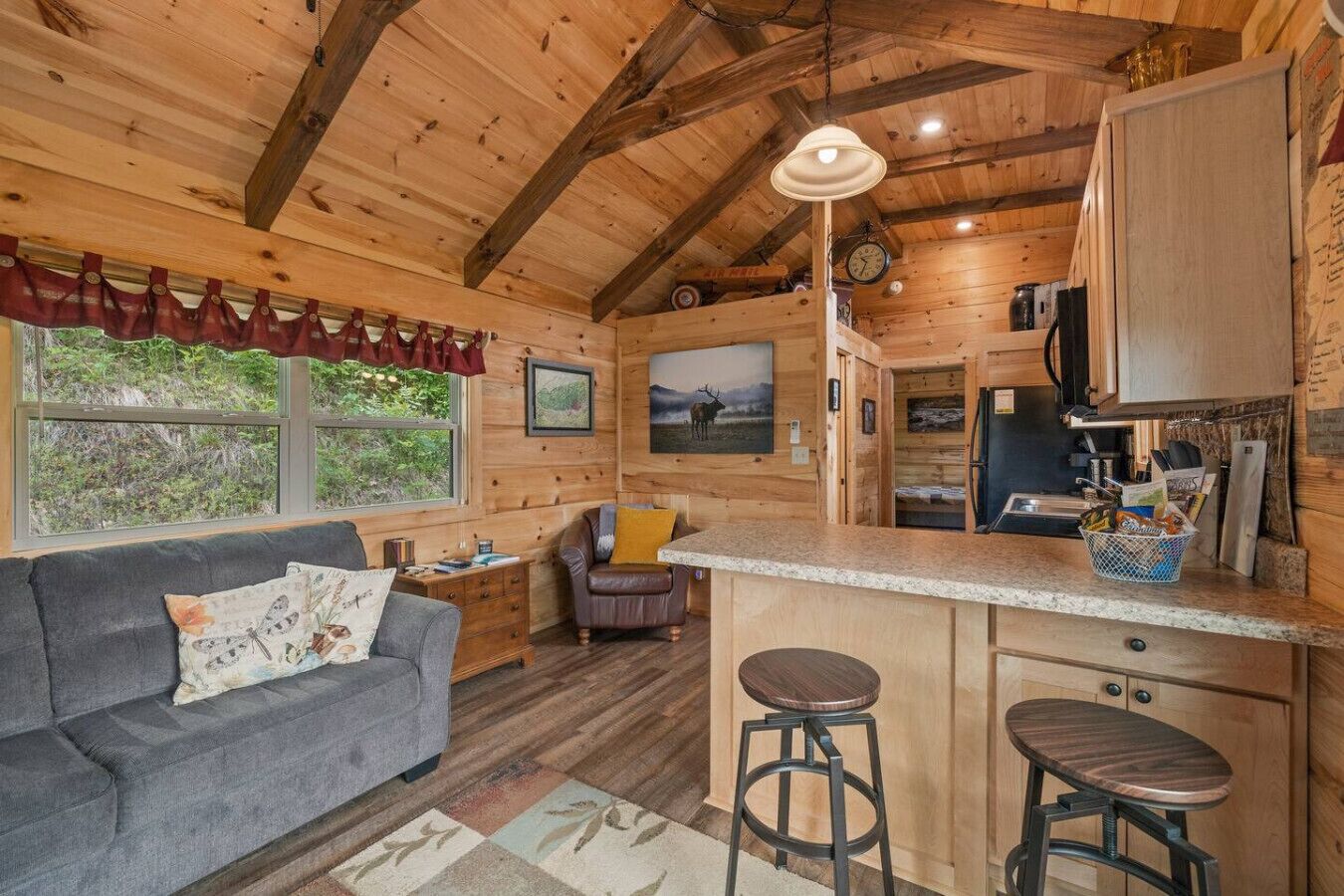 Un interior de cabaña acogedor con un sofá, una zona de comedor, una cocina y un ventanal grande.
