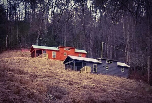 Two houses on a hillside with a forested background.