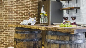 Un coin bar rustique avec un comptoir en bois, deux tonneaux, une bouteille de vin et un verre de vin rouge.