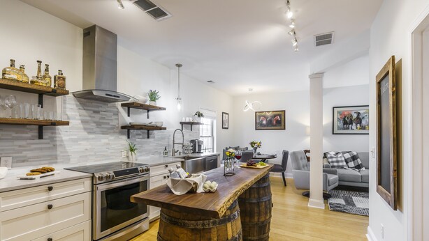 Une cuisine moderne avec un îlot central, des tonneaux en bois et un coin repas comprenant un canapé gris et une table basse.