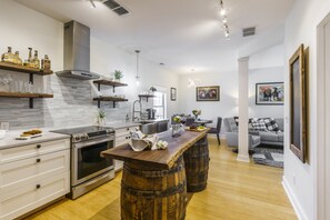 Een moderne keuken met een centraal eiland, houten vaten en een zithoek met een grijze bank en een salontafel.