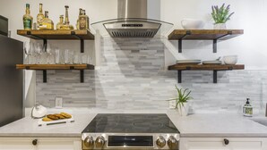 Une cuisine moderne dotée d’une cuisinière en acier inoxydable, d’étagères en verre où sont disposées des bouteilles, et d’un dosseret carrelé.