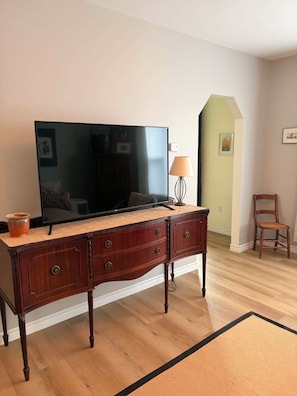 Un salon avec un téléviseur à écran plat posé sur un meuble en bois, une lampe, un fauteuil et un tapis.