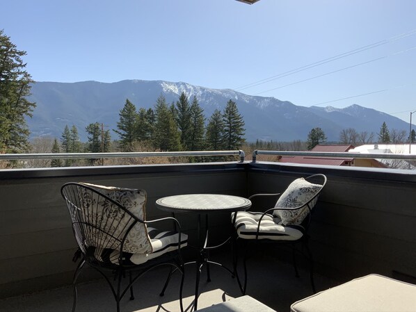 Een balkon met twee stoelen en een kleine tafel, met uitzicht op een bergketen.