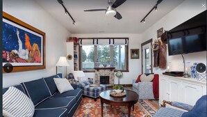 Una sala de estar con sofá, sillón, reposapiés, chimenea, televisión y un cuadro en la pared.