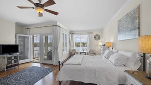 A bedroom with a large bed, a ceiling fan, a TV, and a view through the glass doors. - Waterfront Views & Boat Slip, Blackwell Point #B (Oriental)