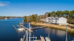 A marina with docked boats, a row of white buildings with large windows, and a clear blue sky. - Waterfront Views & Boat Slip, Blackwell Point #B (Oriental)
