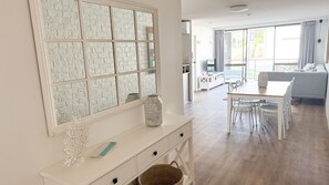 A spacious living area with a large window, a dining table with chairs, a sofa, and a white console table with decorative items.