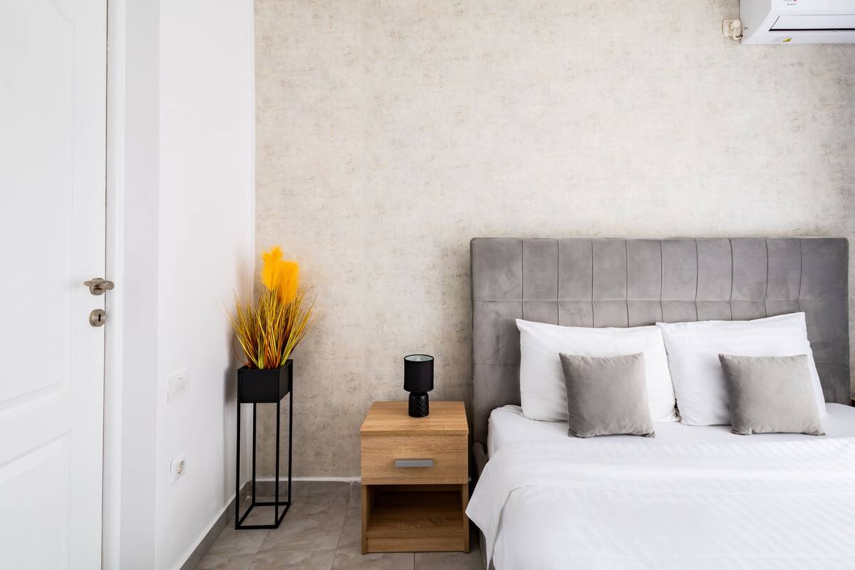 A bedroom with a bed, bedside table, and a wall-mounted air conditioner.