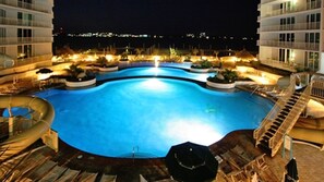 Una piscina con sillas de descanso y sombrillas, rodeada de edificios con balcones.