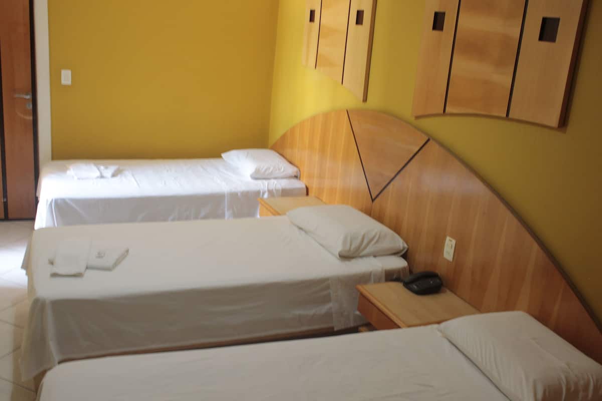 Quarto de hotel com duas camas de solteiro, cabeceiras de madeira e uma pequena mesa de cabeceira com telefone.