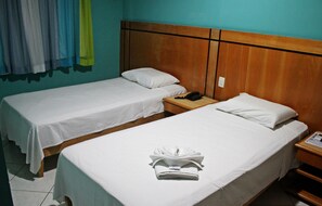 Camera d'albergo con due letti singoli, una testiera in legno, un comodino con il telefono e un asciugamano piegato sul letto.