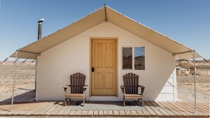 Una cabaña pequeña de un solo nivel con techo a dos aguas, una puerta principal y dos sillas Adirondack en el exterior.