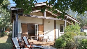 Een houten huis met veranda, een eethoek en twee lounge fauteuils.