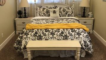A bedroom with a bed, two bedside tables, a bench, a clock, and a window with curtains.