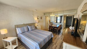 Un dormitorio con cama, mesita de noche, lámpara y vistas al comedor contiguo.