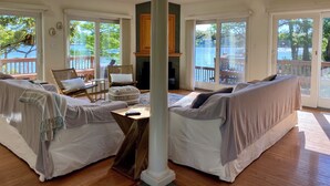 A spacious living room with a high ceiling, skylights, and large sliding glass doors offering views of a lake and deck.