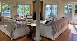 A spacious living room with a high ceiling, skylights, and large sliding glass doors offering views of a lake and deck.