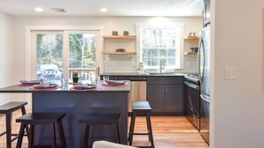 A modern kitchen with dark cabinetry, a central island with stools, and a view of the outdoors through large windows.