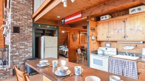 L’intérieur d’un chalet en bois comprend une cuisine, un coin repas et une cheminée.
