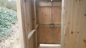 Un sauna en bois au design simple, une pomme de douche en métal et un banc en bois.