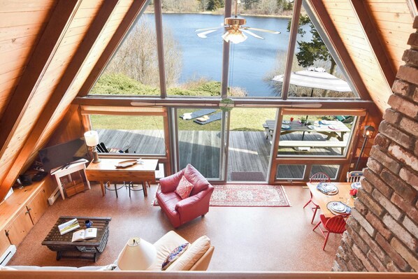 Un loft spacieux doté d’une grande fenêtre donnant sur un lac, et aménagé avec un canapé en cuir, une table et un bureau.