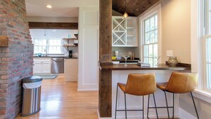 Una cocina moderna con pared de ladrillo, vigas de madera y una barra con dos taburetes.