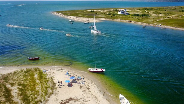 Zona costera con barcos, una playa y un faro.