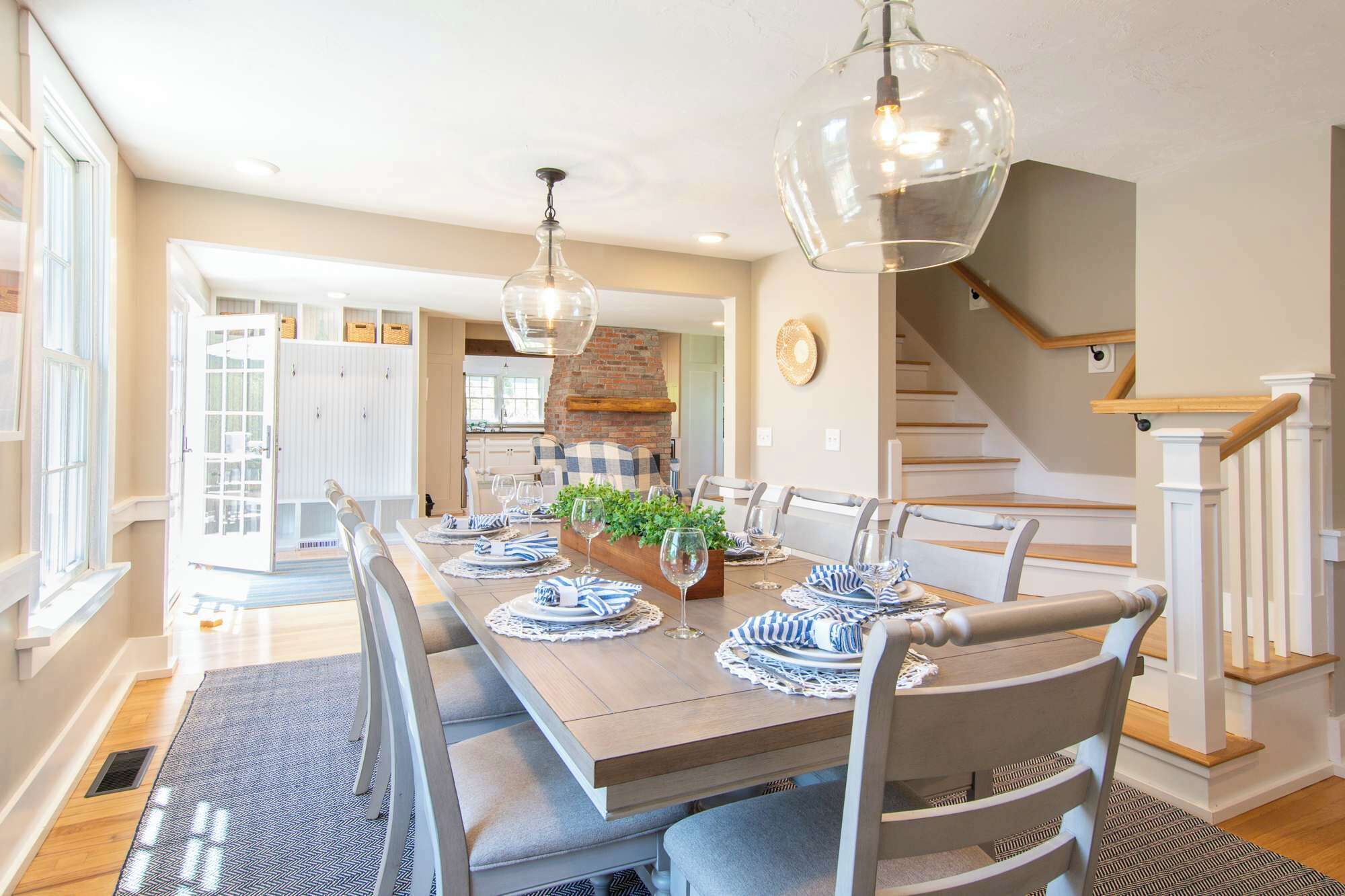 A dining area with a long table set for six, a brick fireplace, and a staircase.