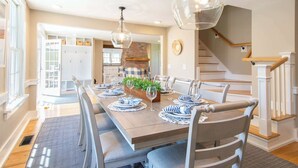 Un comedor con una larga mesa dispuesta para seis personas, una chimenea de ladrillo y una escalera.