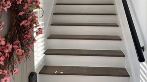 Un escalier aux murs blancs et aux marches en bois foncé, avec une main courante noire et une guirlande décorative sur le côté gauche.