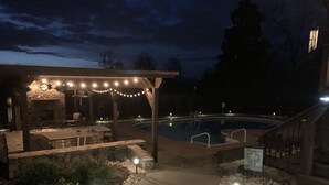 Un espace piscine extérieur doté d’un patio couvert, d’une cheminée en pierre et de guirlandes lumineuses.