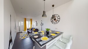 A modern kitchen with a dining area, featuring a large island with a clock and a plant. - Paris House (Villejust)