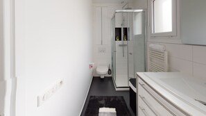 A compact bathroom with a toilet, a glass shower enclosure, a white sink, and a towel rack. - Paris House (Villejust)