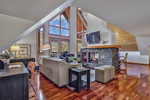 A spacious loft with a high ceiling, a stone fireplace, a large window, and a cozy seating area.