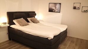 Une chambre à coucher moderne avec une tête de lit sombre, une literie blanche et une table de chevet avec une lampe.