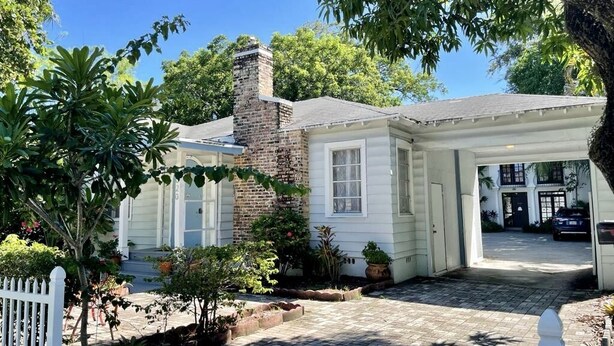 Une maison de plain-pied avec une cheminée en briques, un revêtement extérieur blanc et une véranda.