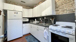 Une cuisine de taille réduite, avec des meubles blancs, un réfrigérateur, un four à micro-ondes, une cuisinière et un évier.