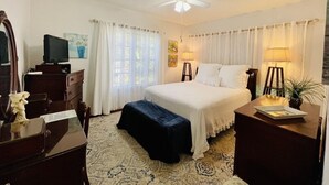 Une chambre à coucher comprenant un lit, des tables de chevet, un bureau, une chaise, un ventilateur de plafond et une fenêtre avec des rideaux.