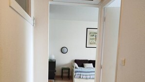 Un pasillo estrecho que conduce a un dormitorio con cama, una mesita y un aire acondicionado instalado en la pared.