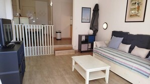 Una sala de estar con sofá, mesa de centro, televisor y una escalera que lleva a otra habitación.