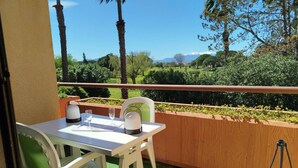 Un balcón con mesa y sillas, con vistas a un jardín ajardinado y montañas distantes.