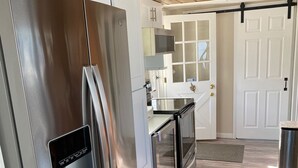 A modern kitchen with stainless steel appliances, white cabinetry, and a wooden floor. - Waterfront Beach House (Clinton)